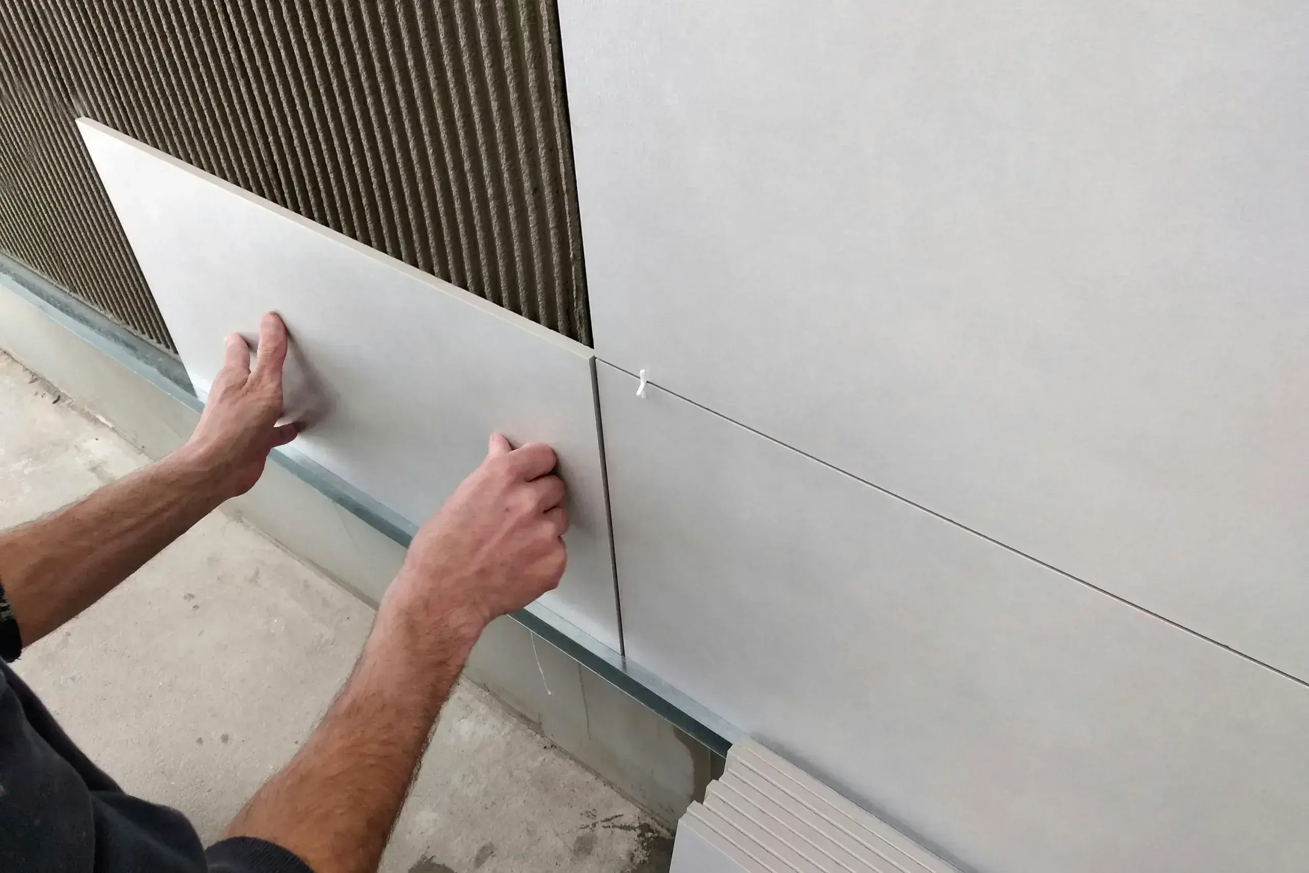 Worker installing white insulation panel against corrugated metal roofing during construction