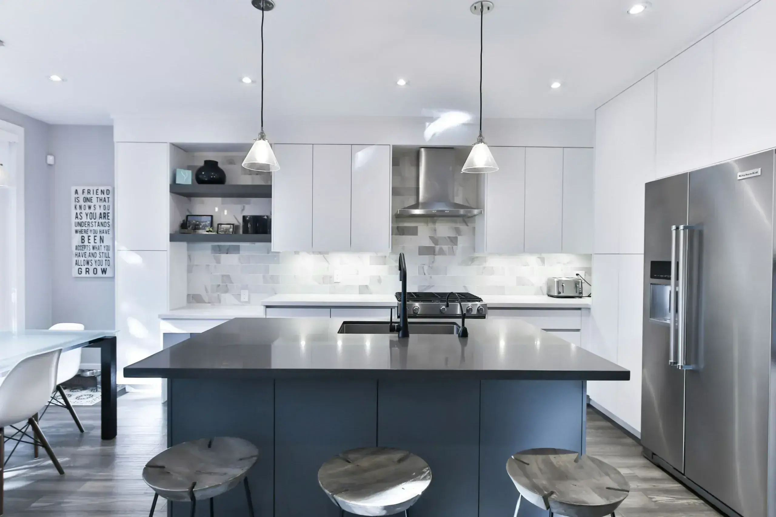 Modern kitchen with white cabinetry, marble backsplash, stainless steel appliances, dark island with black countertop, and pendant lighting