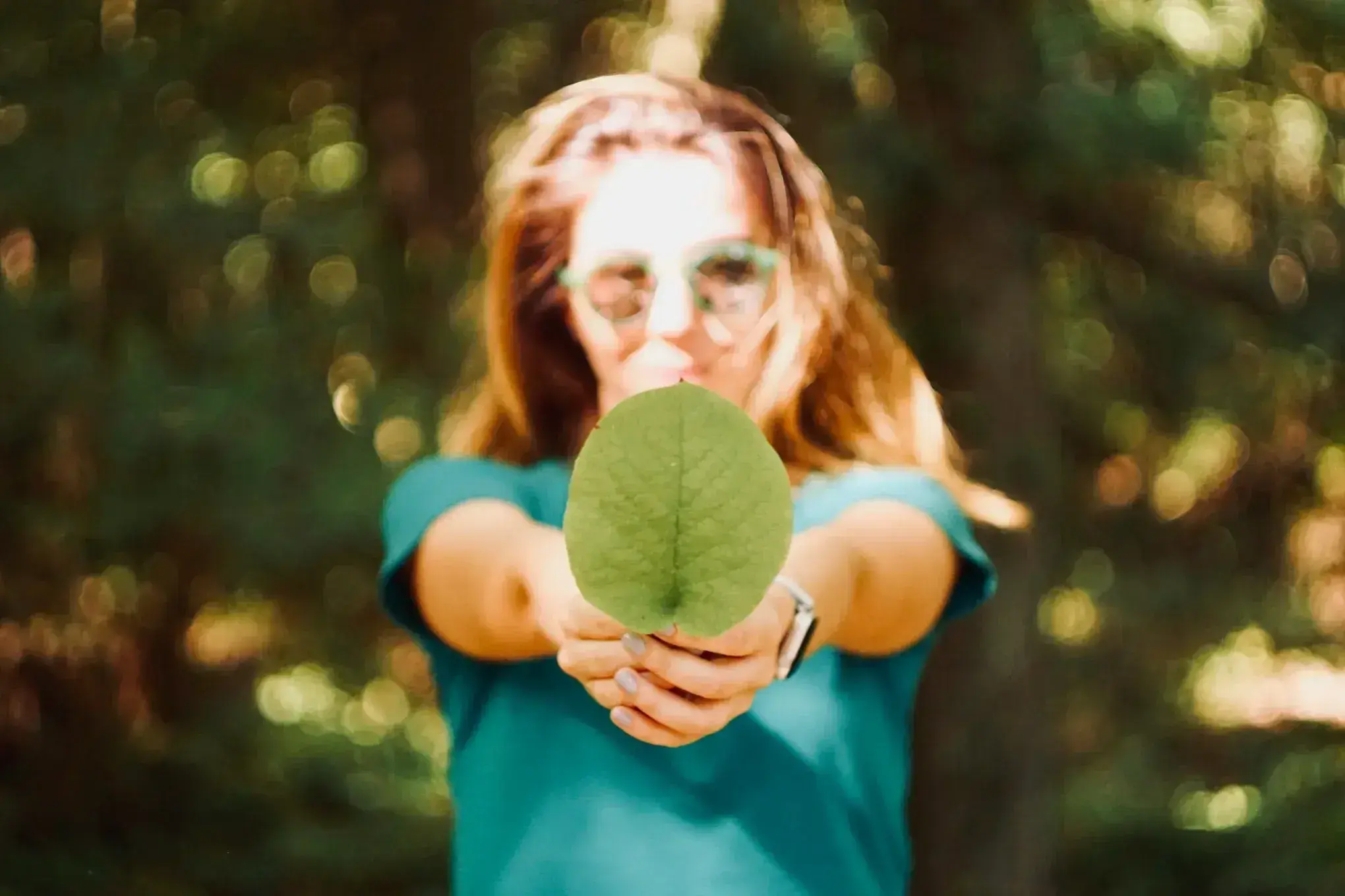 Woman holding a green leaf outdoors with blurred foliage background